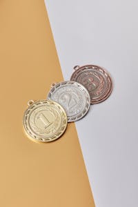 Gold, silver, and bronze medals on a minimalistic beige background.